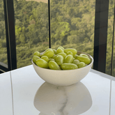 Bowl branco com uvas verdes frescas sobre mesa posta, ideal para servir frutas no café da manhã ou em bandejas decorativas. Combine com taças, xícaras de café e porta temperos para uma cozinha elegante e funcional.